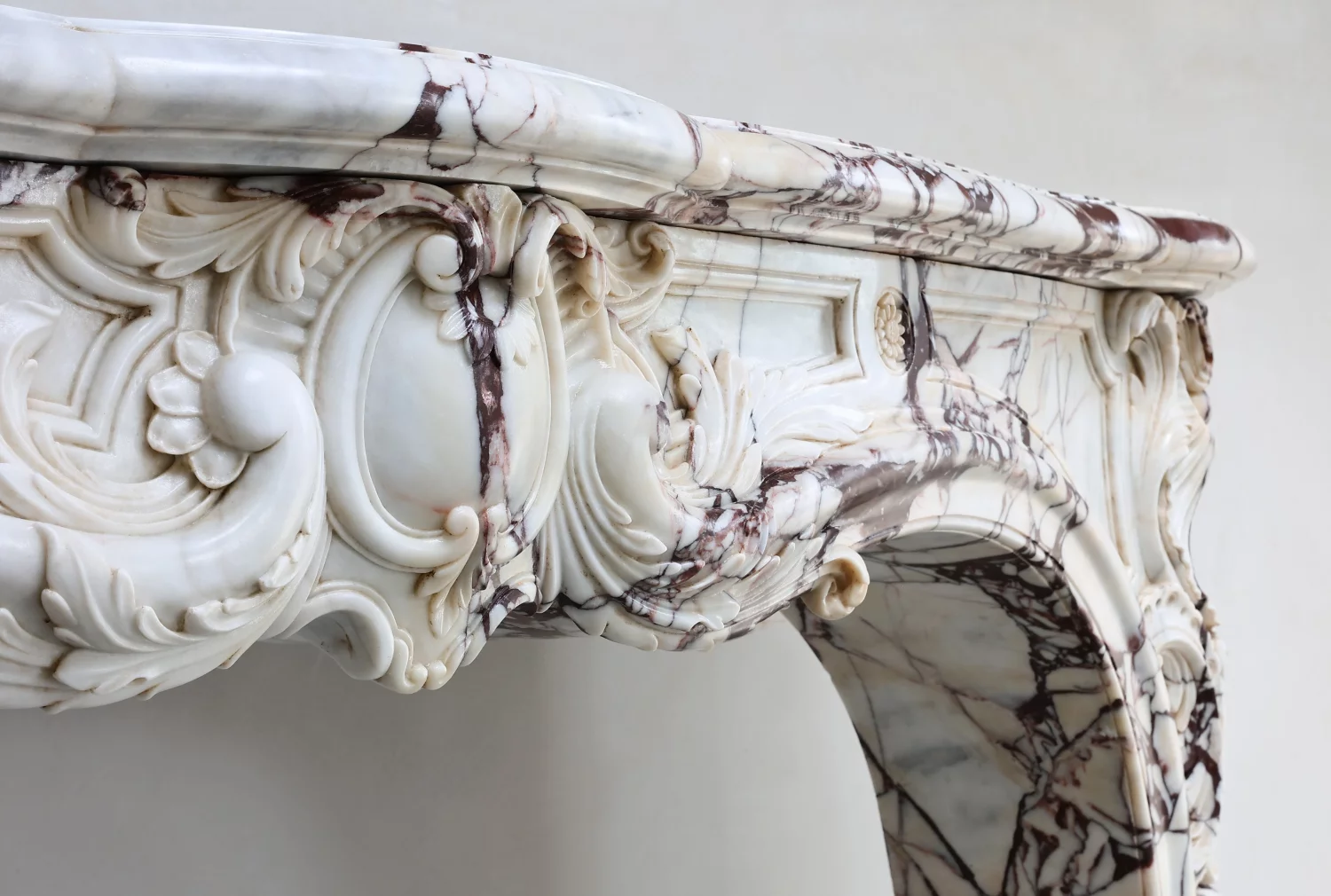 Detailaufnahme antiker Brèche Violette Marmorkamin, Louis-XV Kaminumrandung mit geschwungenem Bogen, Rocaille-Ornamentik, Blütenrosette und violett-brauner Marmoraderung